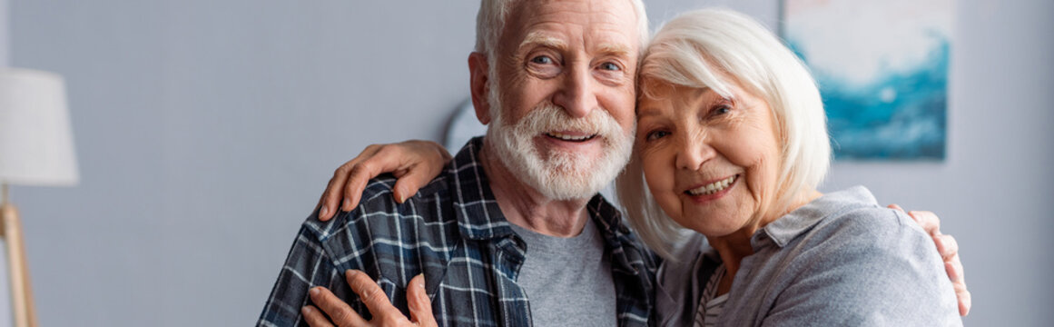 horizontal image of happy senior couple smiling and embracing while looking at camera