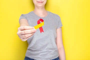 World Hepatitis Day concept. Girl in gray T-shirt holds in her hand awareness symbol red-yellow ribbon. Yellow background