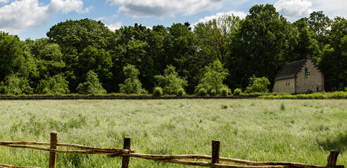 Wide panorama of rural Flemish landscape of pasture with wooden fence an old brick house and a treeline in the background some white clouds