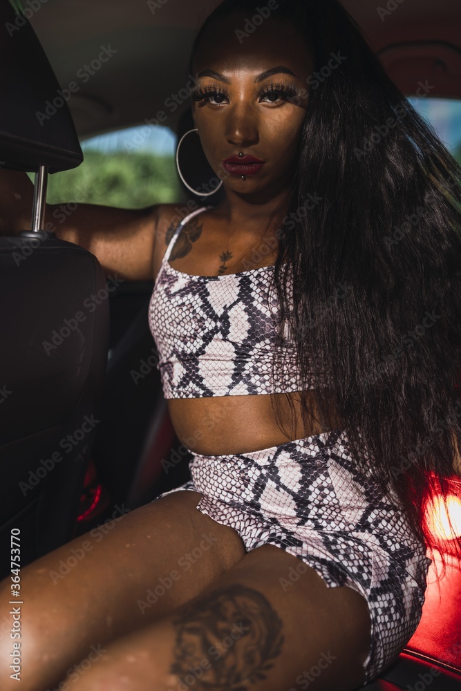 Poster Vertical shot of a sexy African American female with tattoos and piercings posing on a sunny day