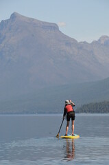 A stand up paddleboarder paddles on Lake McDonald, Glacier National Park, Montana, USA with mountains in the background.