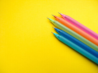 Ballpoint pens of different colors lie on a yellow paper background. Close-up pens with copy space. School and office stationery.