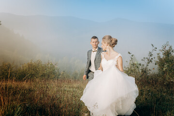 Beautiful wedding couple walk and hold hands during morning trip in mountains.