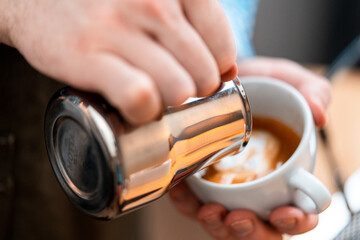 Close Up Of Amateur Barista Hands Pouring Steamed Milk In Homemade Coffee. Making Beautiful Latte Art. Stay Home Concept