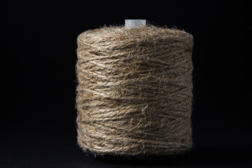 Jute thread on a black background. One spool of jute thread stands in the middle of the frame