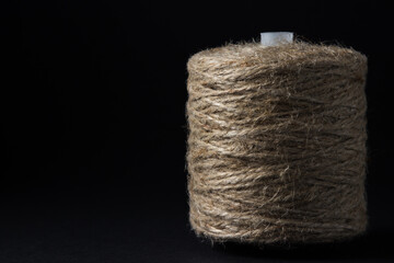 Jute thread on a black background. One spool of jute thread is on the right side of the frame.