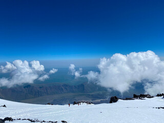Snowy rocky slopes of the northern Elbrus region. Blue sky and mighty white clouds.