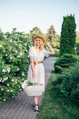 Young beautiful european blonde longhaired girl in white dress and hat at nature. Spends the weekend outside the city, outdoors, a picnic in the park, relaxation, Summer time.
Hold bascet with flowers