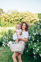 Young and beautiful mother holding baby girl toddler in white dress. Family in park spend time together, tender, love, hugs, play. Stylish summer clothing. 