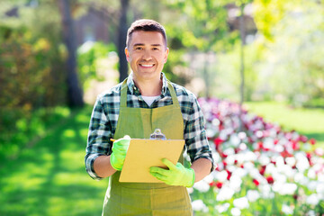 gardening and people concept - happy smiling middle-aged man in apron writing to clipboard at...