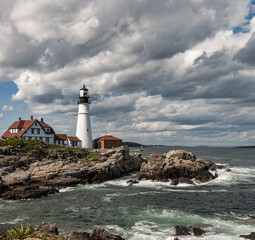 Fototapeta na wymiar Light house on a rocky seacoast with blue sky and white clouds