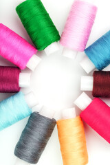Sewing threads of different colors on reels on a white background in a circle.