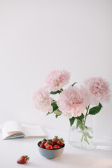 Obraz na płótnie Canvas Pink peonies in a vase and strawberries on white background. Beautiful fresh cut bouquet. Home house interior. Summer wallpaper