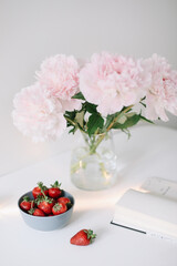Obraz na płótnie Canvas Pink peonies in a vase and strawberries on white background. Beautiful fresh cut bouquet. Home house interior. Summer wallpaper