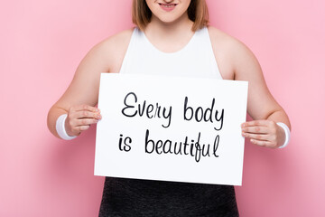 cropped view of smiling overweight girl holding placard with every body is beautiful inscription on...