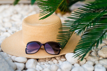 straw hut, sunglasses and palm tree leaves on the pebble beach, vacations concept.