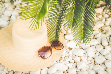 straw hut, sunglasses and palm tree leaves on the pebble beach, vacations concept.