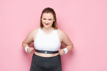 excited overweight girl showing winner gesture on pink