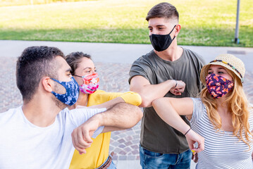 Young friends wearing the protective mask, they greet each other with new greetings, touching...