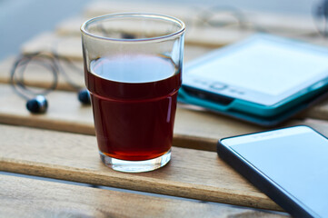 Wooden table with glass of black strong coffee and mobile headphones, smartphone and e-book. Work and study in cafe.