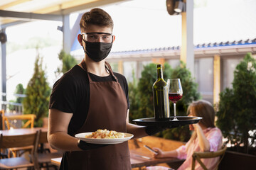 The waiter works in a restaurant in a medical mask, gloves during coronavirus pandemic....