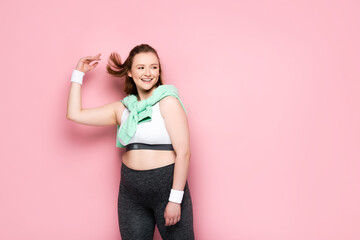 happy overweight girl with sweatshirt over shoulders looking away on pink