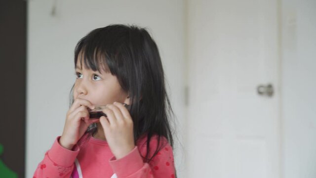 A 4 years old asian little girl is playing harmonica in the morning time, concept of musical education for kid and activity at home for child development.
