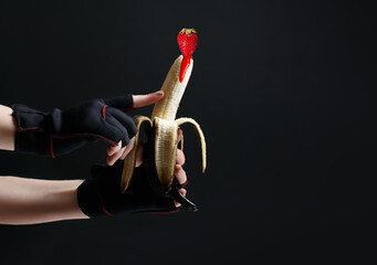 Hands holding a painted black banana on a black background. Concept for sex shops, adult toys