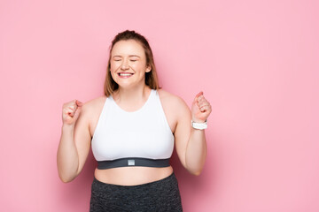 excited overweight girl showing winner gesture on pink