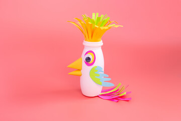 easy parrot craft from paper and recycled yogurt bottle, DIY . Kindergarten or school, creative craft project ideas, pink background