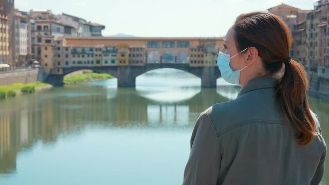 MS Rear view of woman in surgical mask standing in front of Ponte Vecchio / Florence, Tuscany, Italy