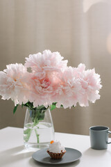 Peony flowers, coffee and cake. Romantic composition. Beautiful pink peonies in a vase at home interior. 