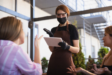 The waitress works in a restaurant in a medical mask, gloves during coronavirus pandemic....