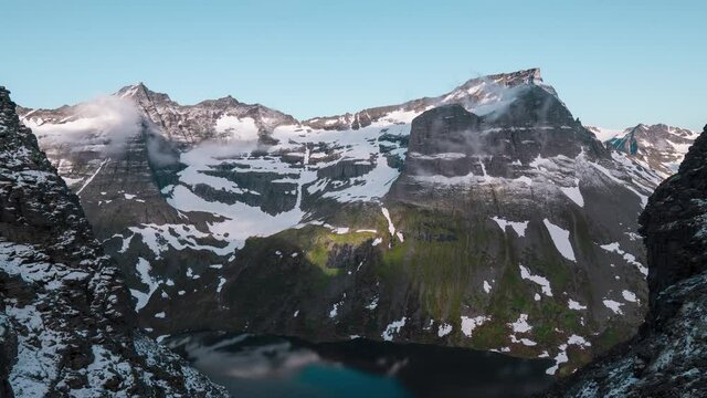 Time lapse of a beautiful scenic view on mountain peaks covered with snow, down in the valley a lake covered in the mountains shadow. No camera movement, shot during day time with a blue sky.