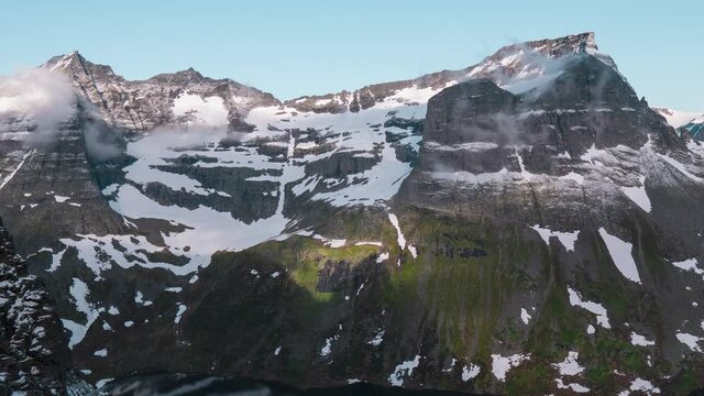 Beautiful scenic time lapse of snow covered mountains, clouds passing by with a shadow covering the lower part of the mountain, camera zooming out.