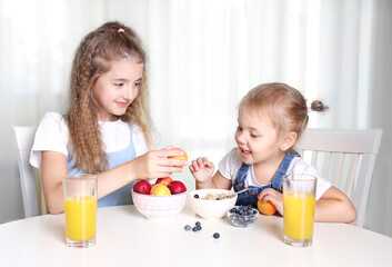 Obraz na płótnie Canvas Two sisters sitting at kitchen table eating fruits.Healthy nutrition concept.Vitamin food.Children have a lunch.Frendship.
