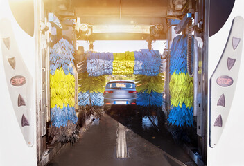 Automatic car washing station with vehicle inside and blue rollers in action. Sunlight effect. Self service