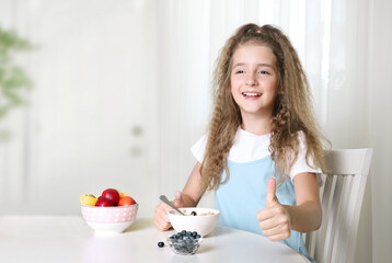 Happy child eating morning breakfast.Kid has fruits and oatmeal for meal.Girl shows finger up.Healthy nutrition concept.