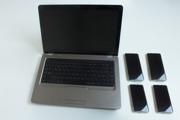 An open laptop computer with four mobile phones on one side on a white background.
