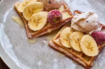 Large gray ceramic plate with fresh Belgian sweet waffles, ice cream, strawberries, bananas and condensed milk. Delicious breakfast and dessert.