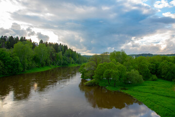  A dark river flows among green banks under a dark, cloudy sky.