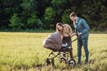 Fototapeta premium Happy parents with love and tenderness look at their child who is lying in a stroller