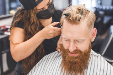 Fototapeta premium Men's haircut in a barbershop. Hair care. Barber in mask protecting from virus. Haircut in quarantine.