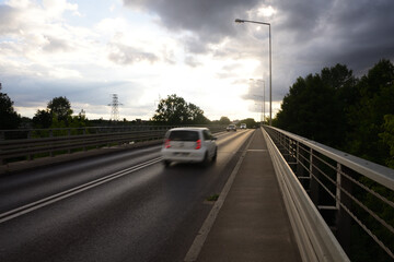 Blurry silhouettes of cars on the bridge against the background of clouds in the blue sky.