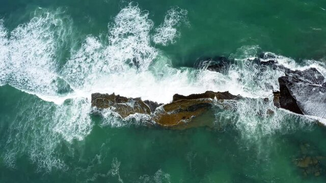 Beautiful bird's eye top aerial drone static shot of waves crushing into a black rock in the beach at Sibauma creating a natural swimming pool during low tide near Pipa in Northern Brazil.