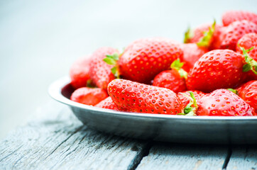 Bright strawberries in a plate on a wooden table