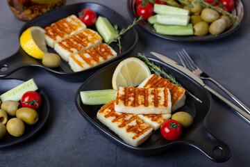Grilled haloumi cheese on a black pan with olives, tomatoes, cucumbers and pepperoni. Close-up.