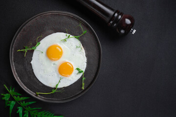 Breakfast with two fried eggs and herbs on black background