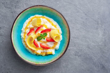 Bowl of milk rice porridge with strawberries, mangoes, honey, mint