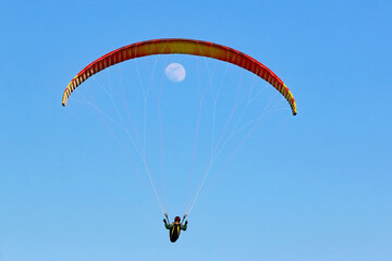 Paraglider flying wing in a blue sky with the moon	